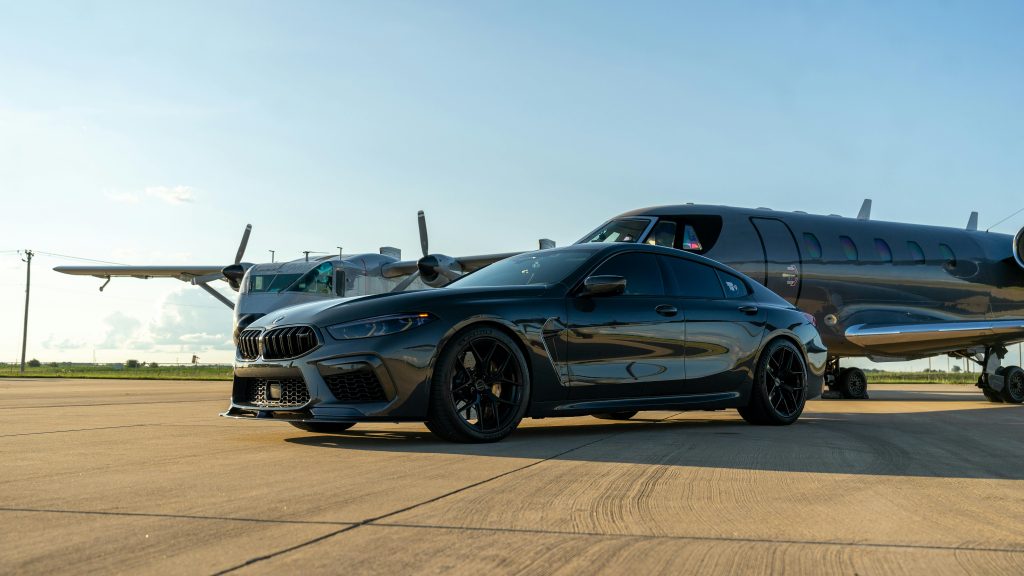 Luxury black car parked alongside a sleek private jet on a sunny airport tarmac.